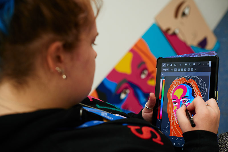 Female student drawing colourful graphical illustration of a woman using a tablet device.