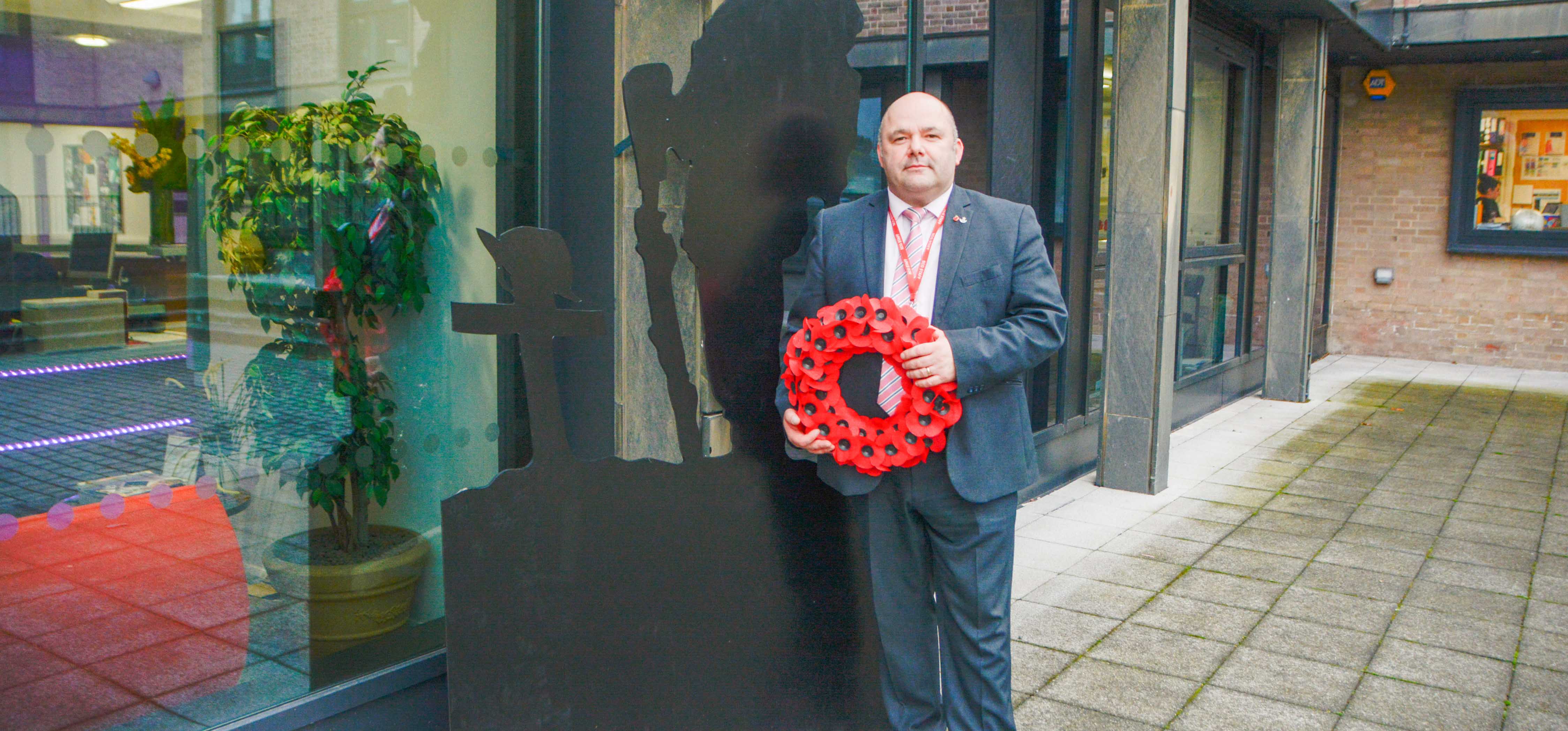 College Commercial Manager holding a poppy wreath and standing next to wooden silhouette of a soldier.