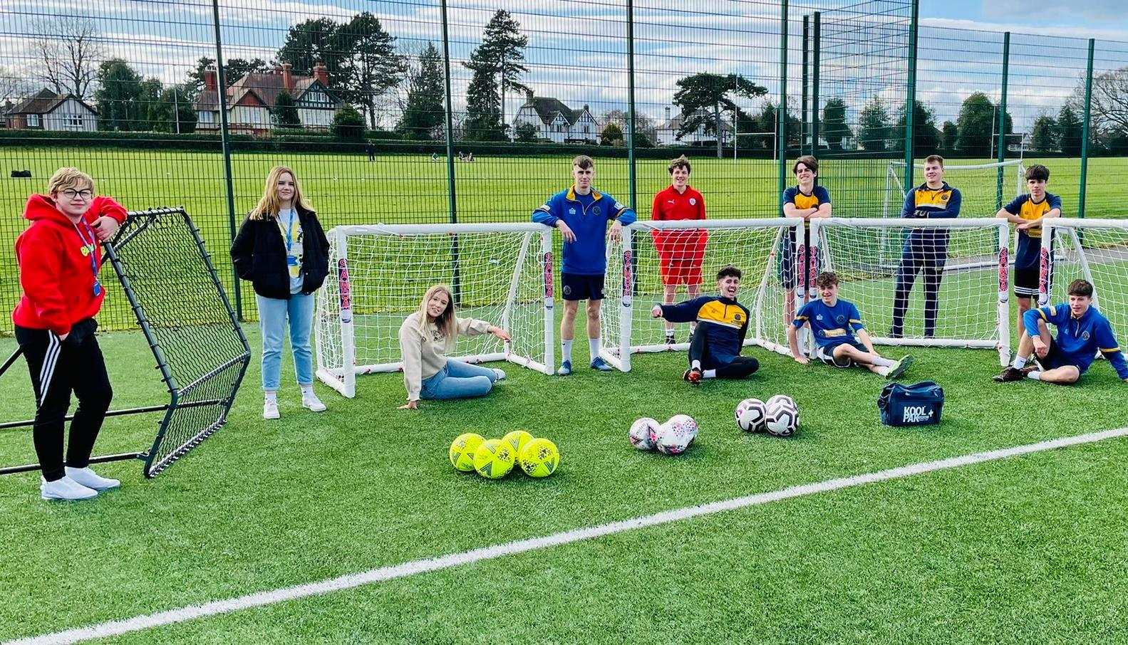 Group of football students posing next to football goals and footballs