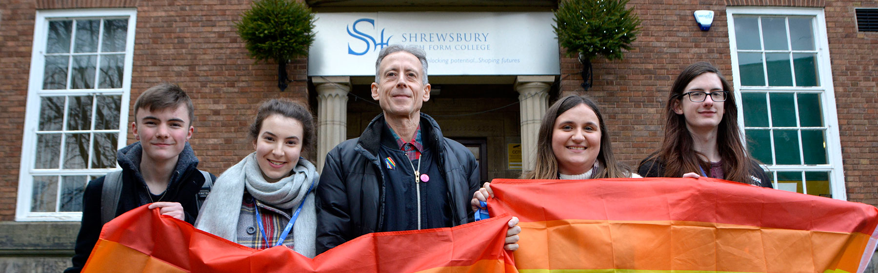 Students and a speaker holding a rainbow flag in the college grounds