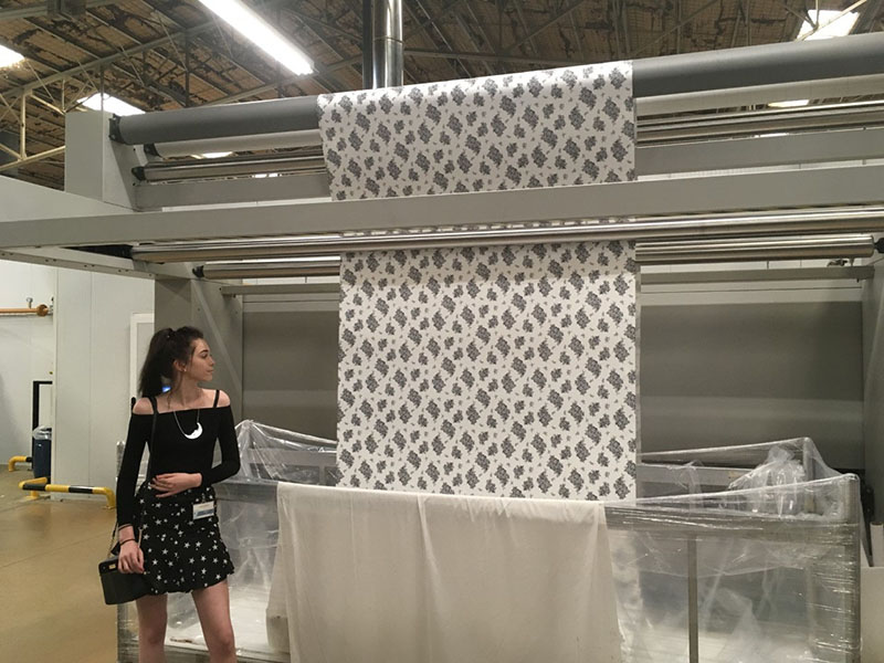 Art and design student standing in front of fabric printing press with her design being printed.