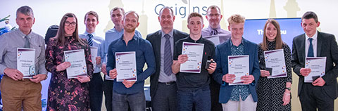 Large group of apprentices holding certificates either side of the College’s Head of Apprenticeships.